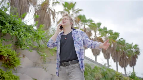 A young man uses his cell phone surrounded by lush palm trees, embodying a Video stock 281609112