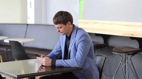 A young man uses his mobile device in a cafe Video stock 73965406