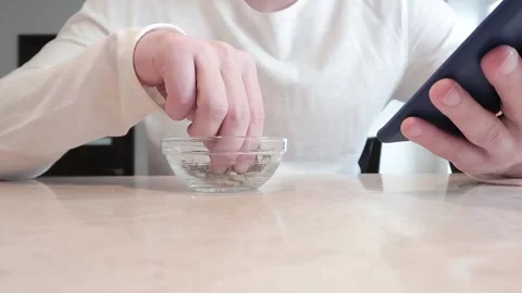 A young man uses a smartphone during break. Pumpkin seeds in transparent bowl Vídeo Stock 131173930