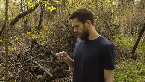 Young man uses a smartphone in a spring forest Stock Footage 80695942