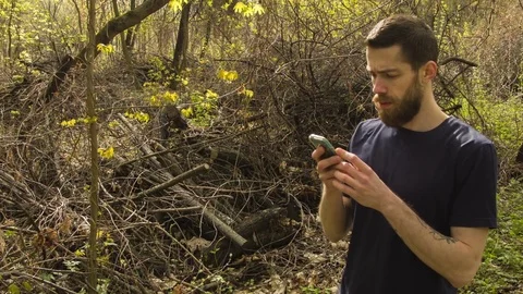 Young man uses a smartphone in a spring forest Video stock 80697387