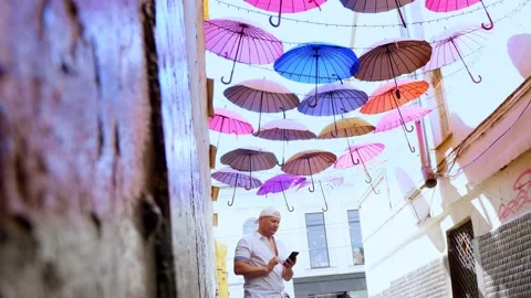 A young man uses a smartphone while standing in a street decorated with colorful Stock Footage 137239596