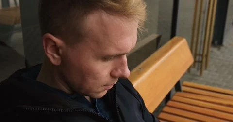 A young man uses a smartphone while sitting at a bus stop Stock Footage 274093214