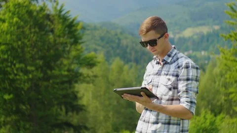 A young man uses a tablet, stands in a picturesque place against a background of Stock Footage