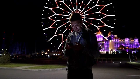 A young man uses a telephone for communication on a background of a ferris wheel Video stock 116781953