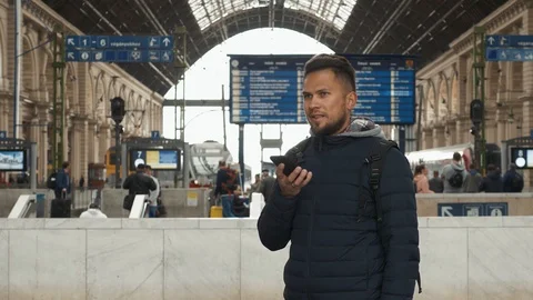Young man uses voice recognition with smartphone at railway station Stock Footage 106523141