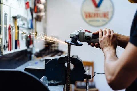 Young man using angle grinder on metal in workshop, cropped Foto stock