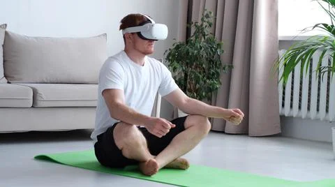 Young man using AR while meditating sitting in lotus position on roll mat Foto stock