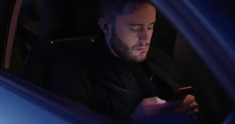 Young man using cell phone while sitting in car driving seat at night Stock Footage 143192537