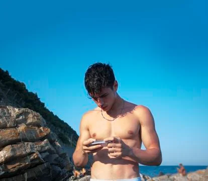 Young Man Using Cell Phone Standing at Beach Boulders Stock Photos