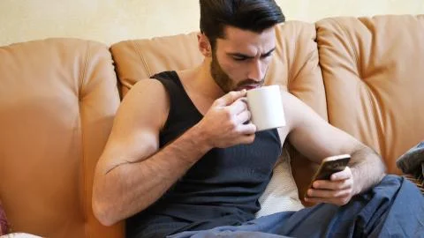 Young man using cell phone while drinking coffee Stock Photos