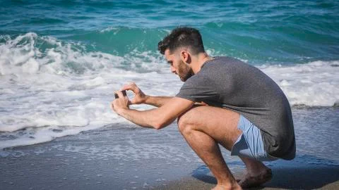 Young man using cell phone to take photo at beach Stock Photos