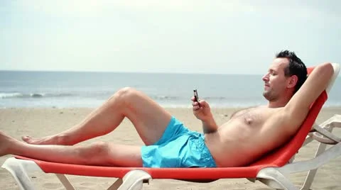 Young man using cellphone while lying on sunbed on beach HD Stock Footage 10851279