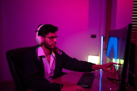 Young man using a computer in a dimly lit room with vibrant purple lighting.. Foto stock