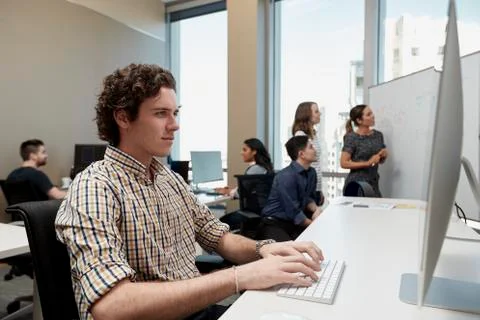 Young man using computer in office looking, co-workers having discussion in 库存照片