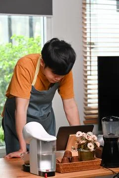 Young man using computer tablet and making coffee with a coffee machine. Stock Photos