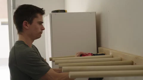 Young man using cordless screwgun on garage rack Stock Footage 298373567