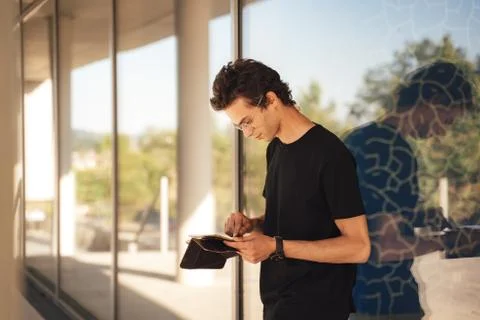 Young man using digital tablet while standing against glass window at college Stock Photos