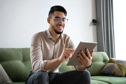 Young man using digital tablet computer sitting on sofa at home office Stock Photos