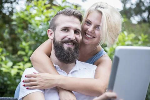 Young man using digital tablet with his girlfriend embracing from behind in gard Stock Photos