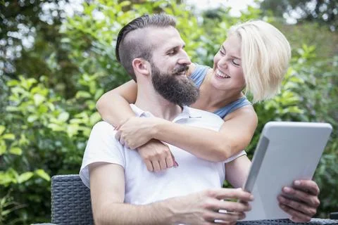 Young man using digital tablet with his girlfriend embracing from behind in gard 스톡 사진