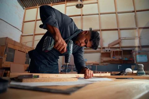 Young man using drill on wood during work at woodworking factory Stock Photos