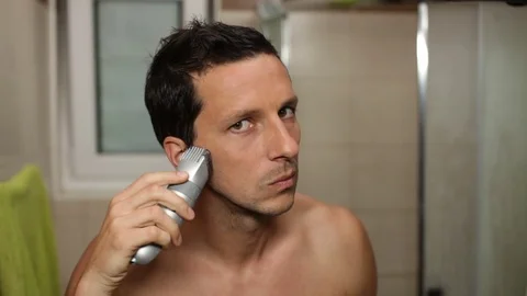 Young man using electric shaver in the morning while looking at himself in the b Stock Footage 79491703