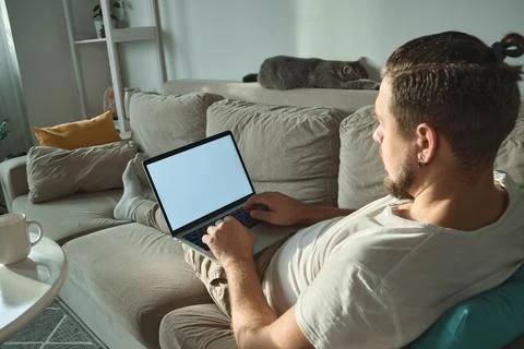 Young man using empty blank screen laptop typing and working lying on the couch Stock Photos