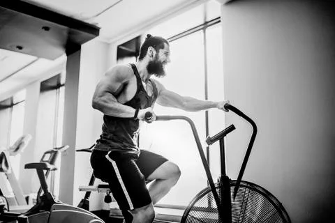 Young man using exercise bike at the gym. Fitness male using air bike for cardio Stock Photos