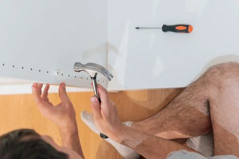 Young man using a hammer to assemble a new closet in the bedroom of his new home Foto stock