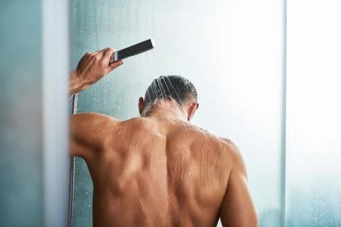 Young man using handheld shower head while washing himself in bathroom Foto stock