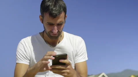 Young man using his cell phone on the beach Stock Footage 52257901