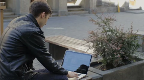 Young man using his laptop on a street bench.man typing on his laptop Video stock 62931711