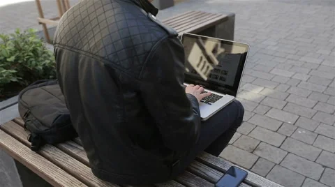 Young man using his laptop on a street bench.man typing on his laptop Stock Footage 62931783