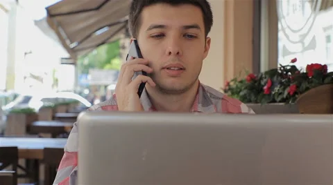 Young man using his laptop in cafe and talking on smartphone smiling happy Stock Footage 62932127