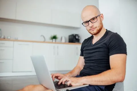 Young man is using his laptop pc and sitting in the kitchen. Stock-Fotos