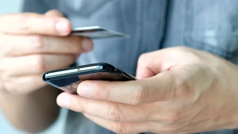 The young man using his phone, a smartphone, and holding a credit card online To Stock Footage 135623827