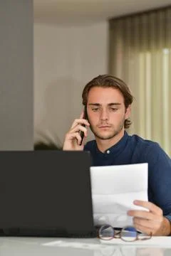 Young man using his phone while holding and looking at an out of focus bill Stock Photos