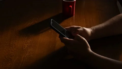 Young man using his smartphone on a wooden table while drinking coffee Stock Footage 139650265
