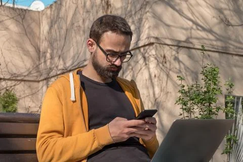 Young Man Using His Smartphone and Laptop Outdoors Stock Photos