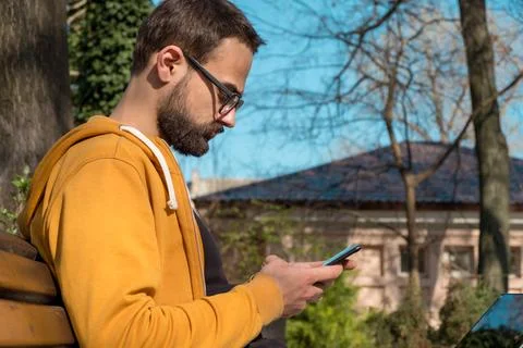 Young Man Using His Smartphone and Laptop Outdoors. Side View. Stock Photos