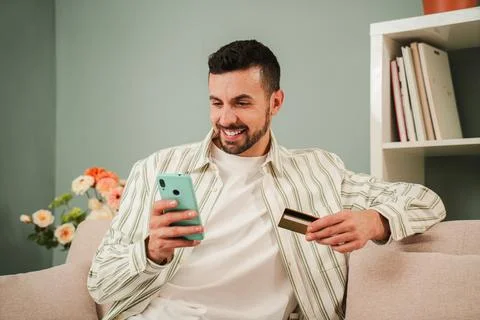 Young man using his smartphone for online shopping, holding a credit card a.. Stock Photos