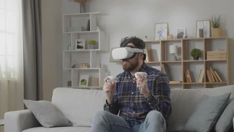 Young man using his VR headset and controller for playing games in the living Stock Footage 169320978