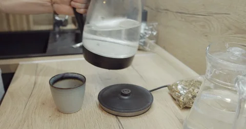 Young man using a kettle in the kitchen to boil water for tea or coffee  Stock Footage 129855385