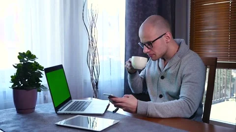 Young man using laptop and mobile phone. He is drinking coffee. Green screen. Stock Footage 61281506