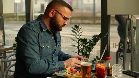 Young man using laptop and drinking beer sitting in restaurant in city  Stock Footage 70999437