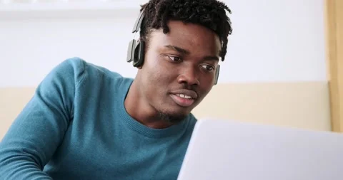 Young man using laptop and listening music on headphones in bedroom Stock Footage 156521327