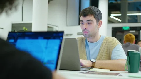 Young Man Using Laptop and Speaking with Colleague in the Office Stock Footage 243988368