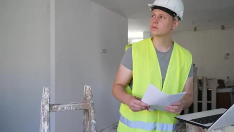 Young man using laptop and verifying papers on part time job in construction Stock Footage 265830044