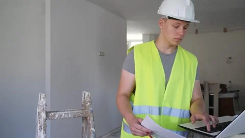 Young man using laptop and verifying papers on part time job in construction Stock Footage 322121536